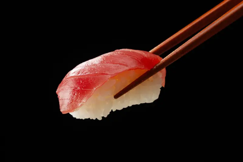 Tuna nigiri sushi held by chopsticks