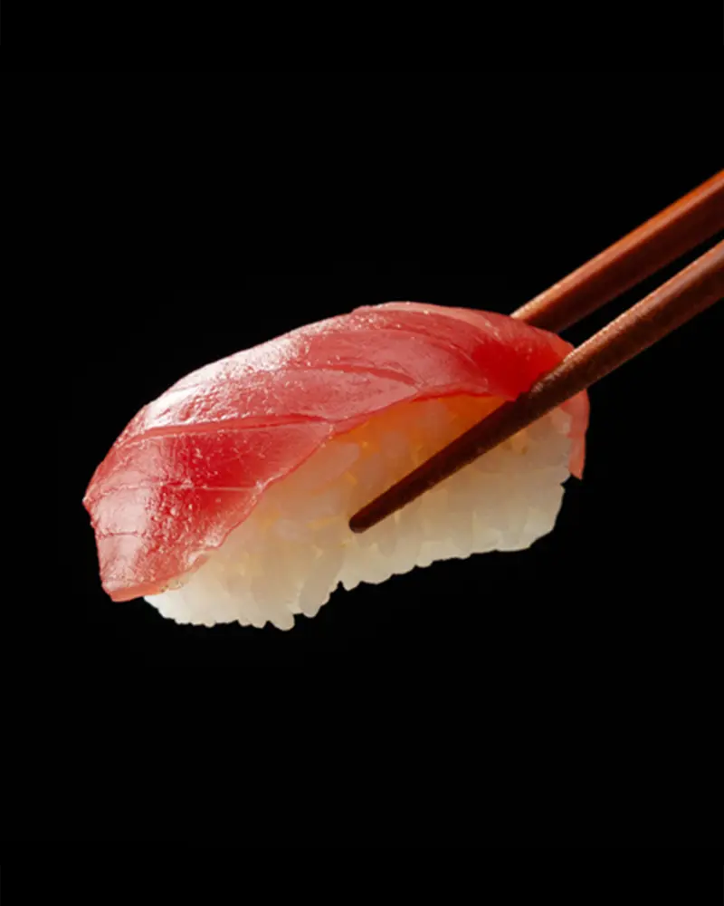 Tuna nigiri sushi held by chopsticks